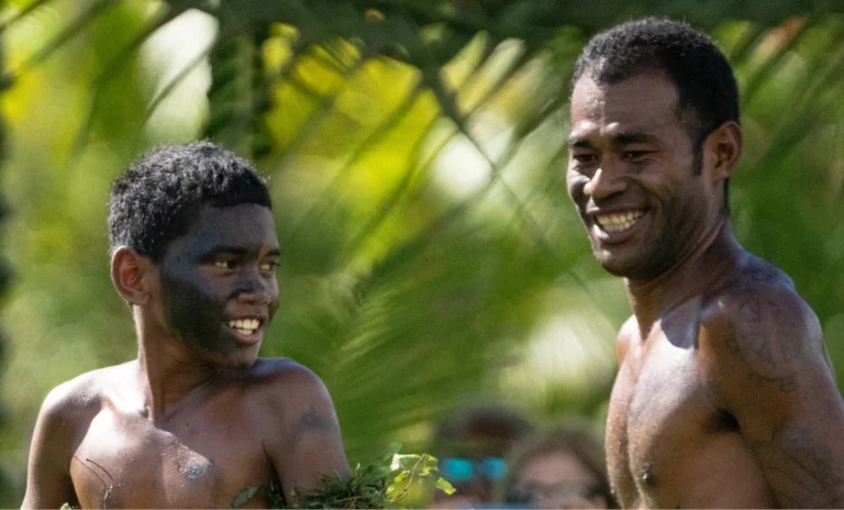 Two smiling Fijian locals standing outdoors surrounded by tropical greenery