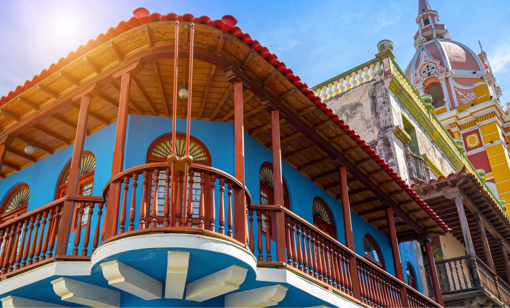 A bright blue colonial-style building with an ornate wooden balcony under a warm sunlit sky.