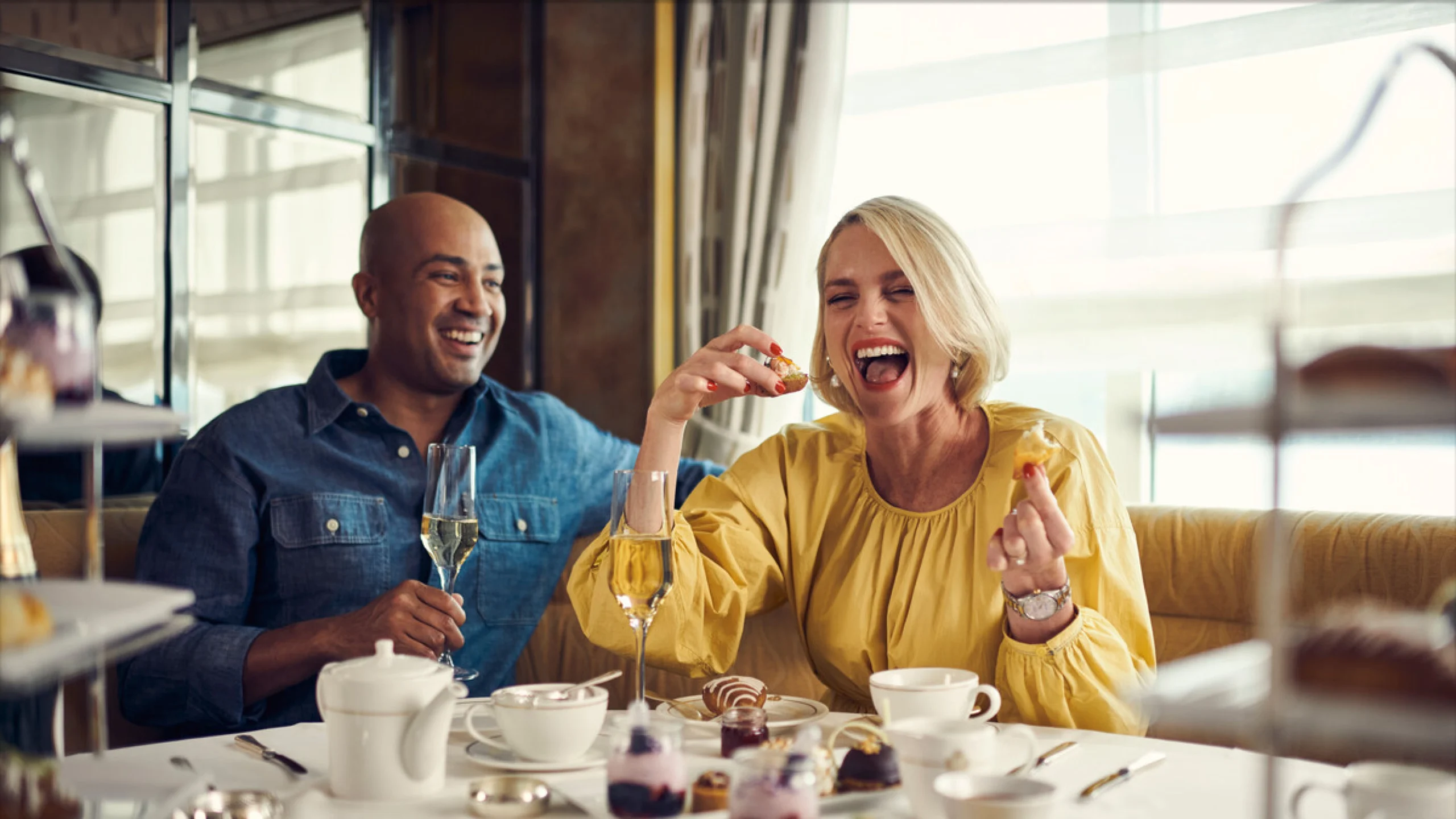 Cunard - A group of friends smiling and enjoying a traditional Afternoon Tea service with tiered dessert stands.