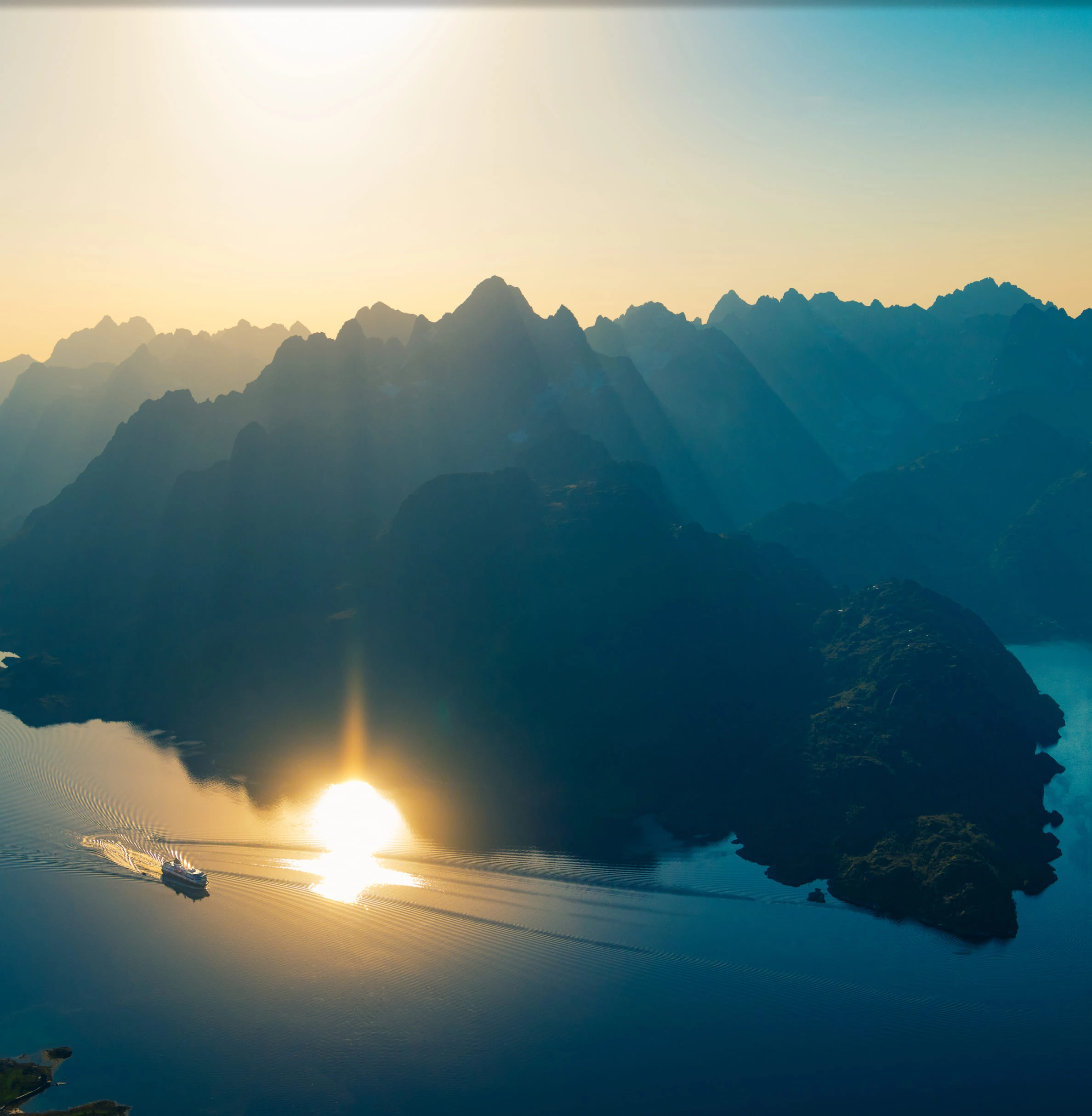 A lone ship in a vast, sunlit fjord surrounded by massive Arctic mountains.