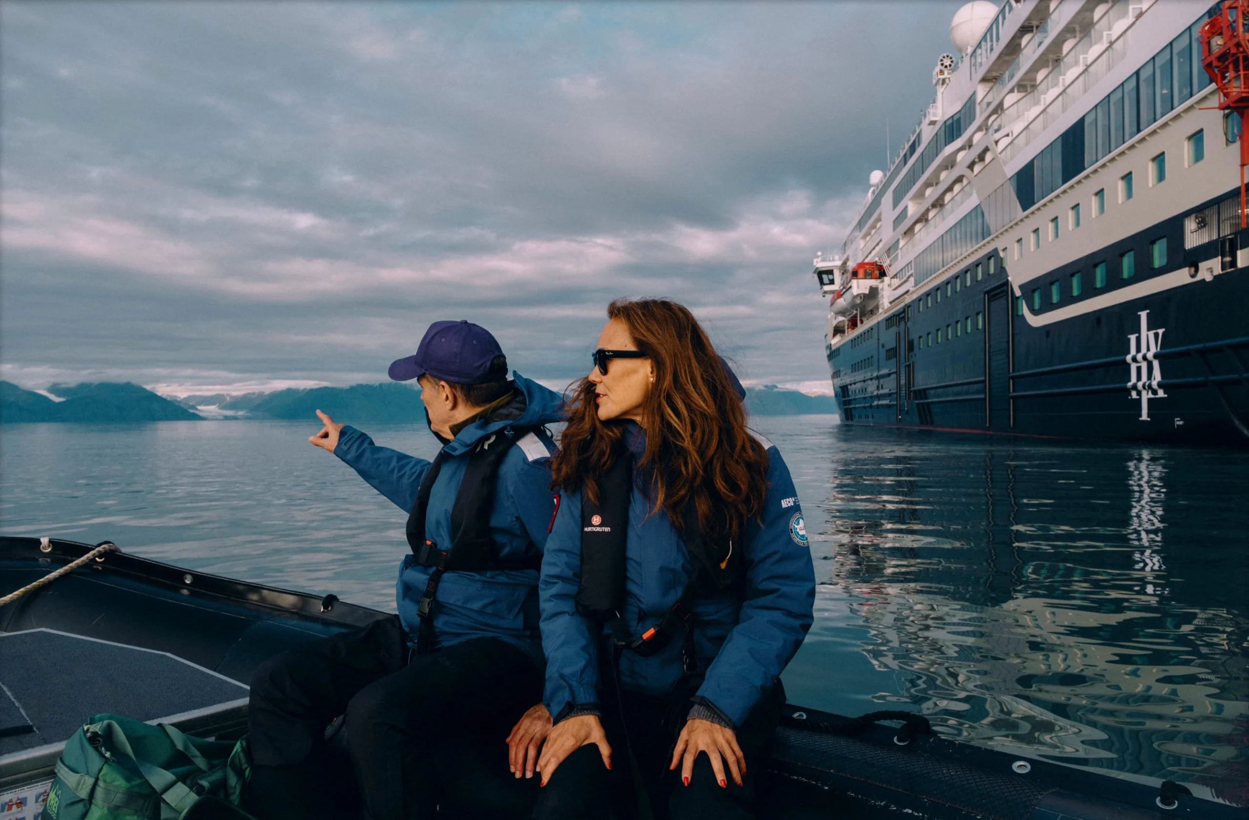 Two guests in blue HX jackets sitting on deck watching the horizon.