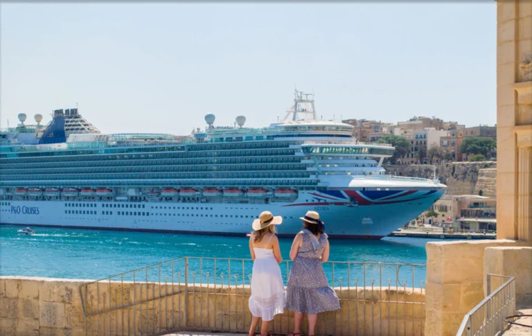 A large cruise ship docked at a historic stone port under a clear blue sky.