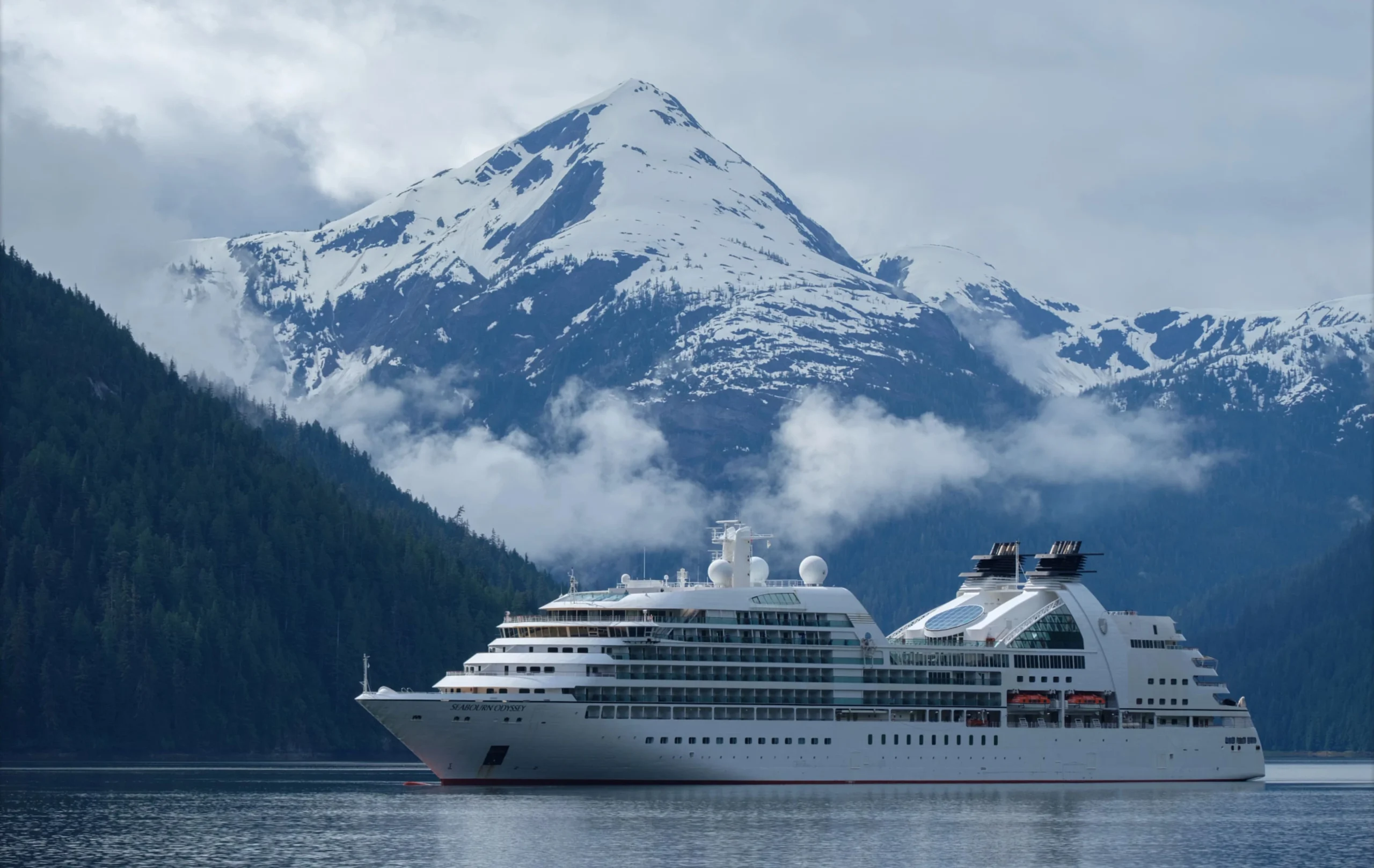 Seabourn luxury cruise ship sailing past snow-capped mountains.