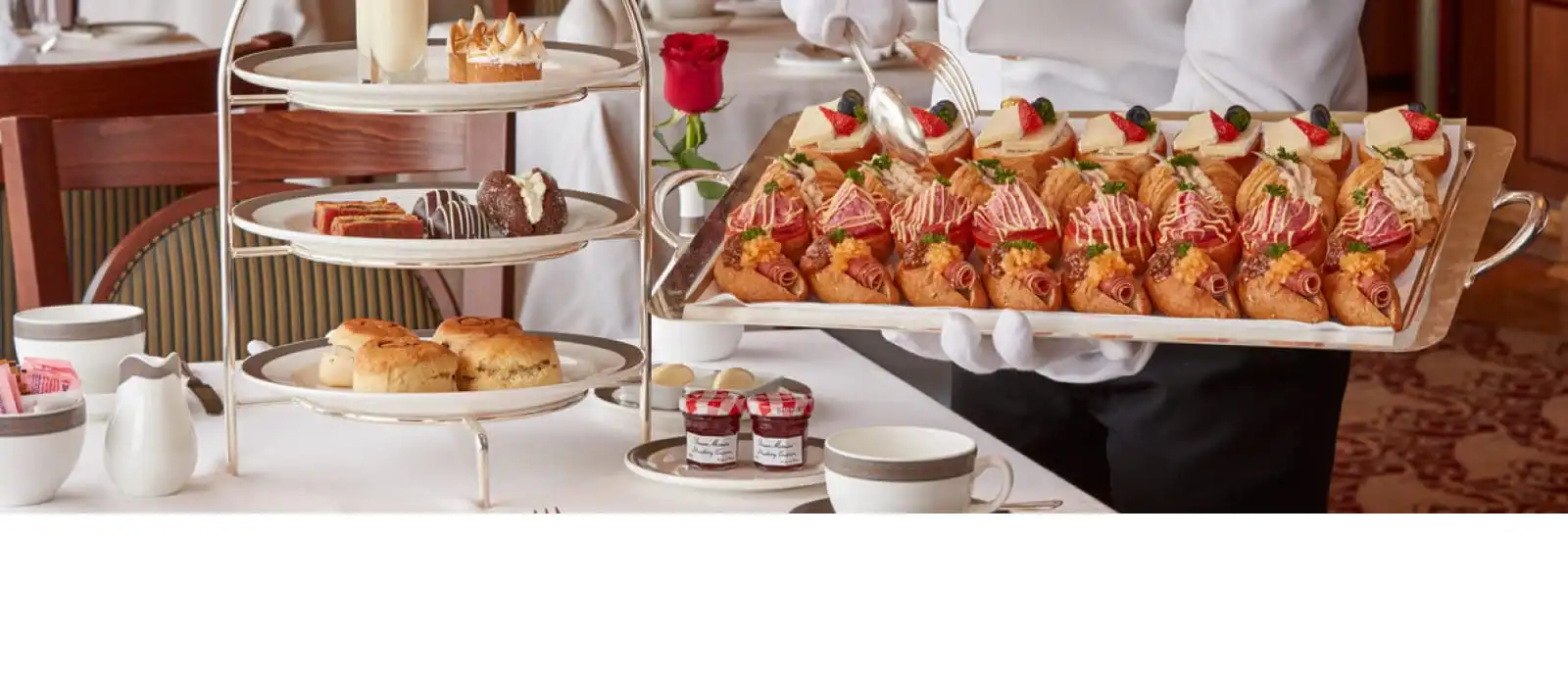 White-gloved waiter serving traditional afternoon tea with pastries and scones aboard Cunard.