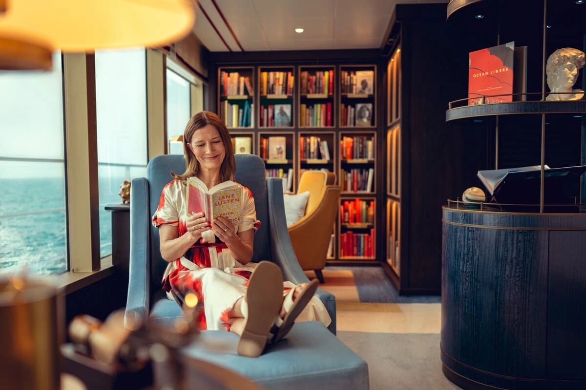 Guest relaxing with a book in a luxurious Cunard lounge overlooking the ocean during an iconic cruise voyage.