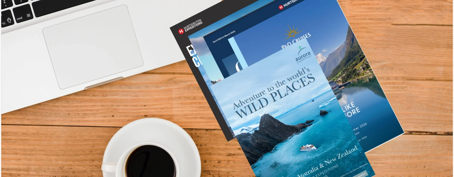 A collection of luxury travel e-brochures featuring expedition cruises and adventure destinations, displayed on a wooden desk beside a laptop and coffee cup.