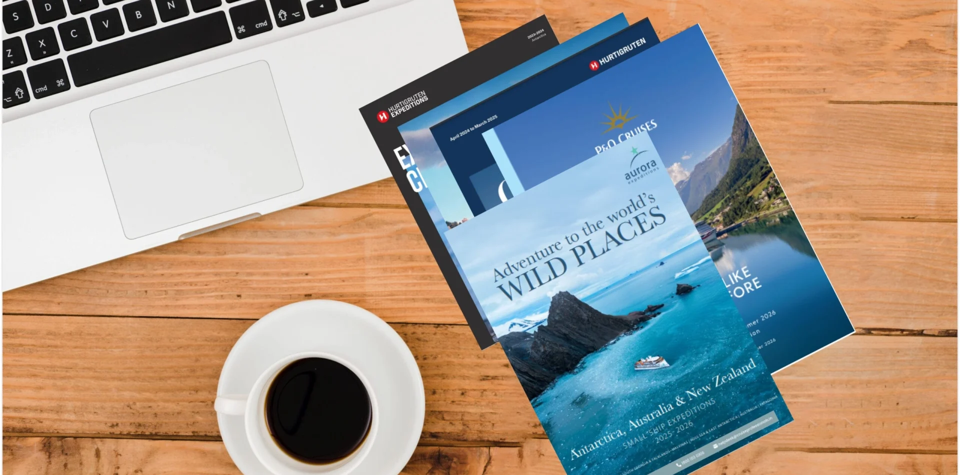 A collection of luxury travel e-brochures featuring expedition cruises and adventure destinations, displayed on a wooden desk beside a laptop and coffee cup.