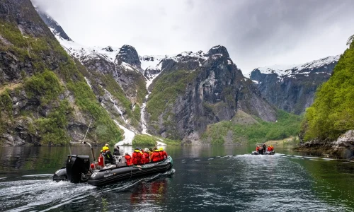 Zodiac boat carrying cruise passengers through a scenic mountain fjord during a guided shore excursion.