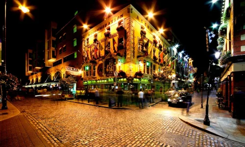 Vibrant night view of The Oliver St. John Gogarty pub in Dublin’s Temple Bar district, featuring illuminated cobblestone streets, historic Irish architecture, and crowds enjoying Dublin nightlife.